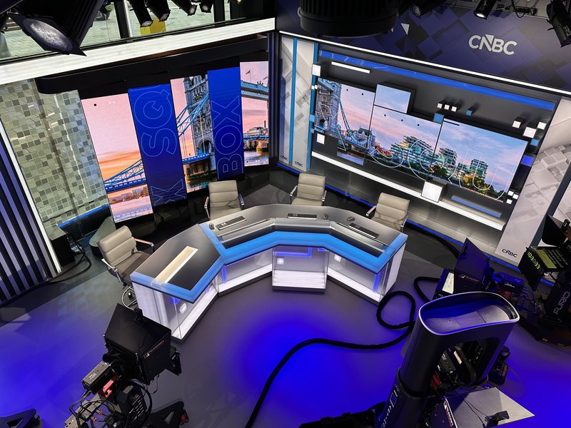 Nachrichtenstudio von CNBC in London: Moderationstisch mit blau leuchtender Kante, dahinter Bildschirme mit der Tower Bridge und dem Schriftzug „Squawk Box“.